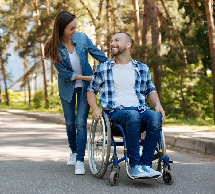Person holding a casserole dish in a kitchen, smiling. Chain necklace, dark shirt. — VAL Disability Services in Taree, NSW
