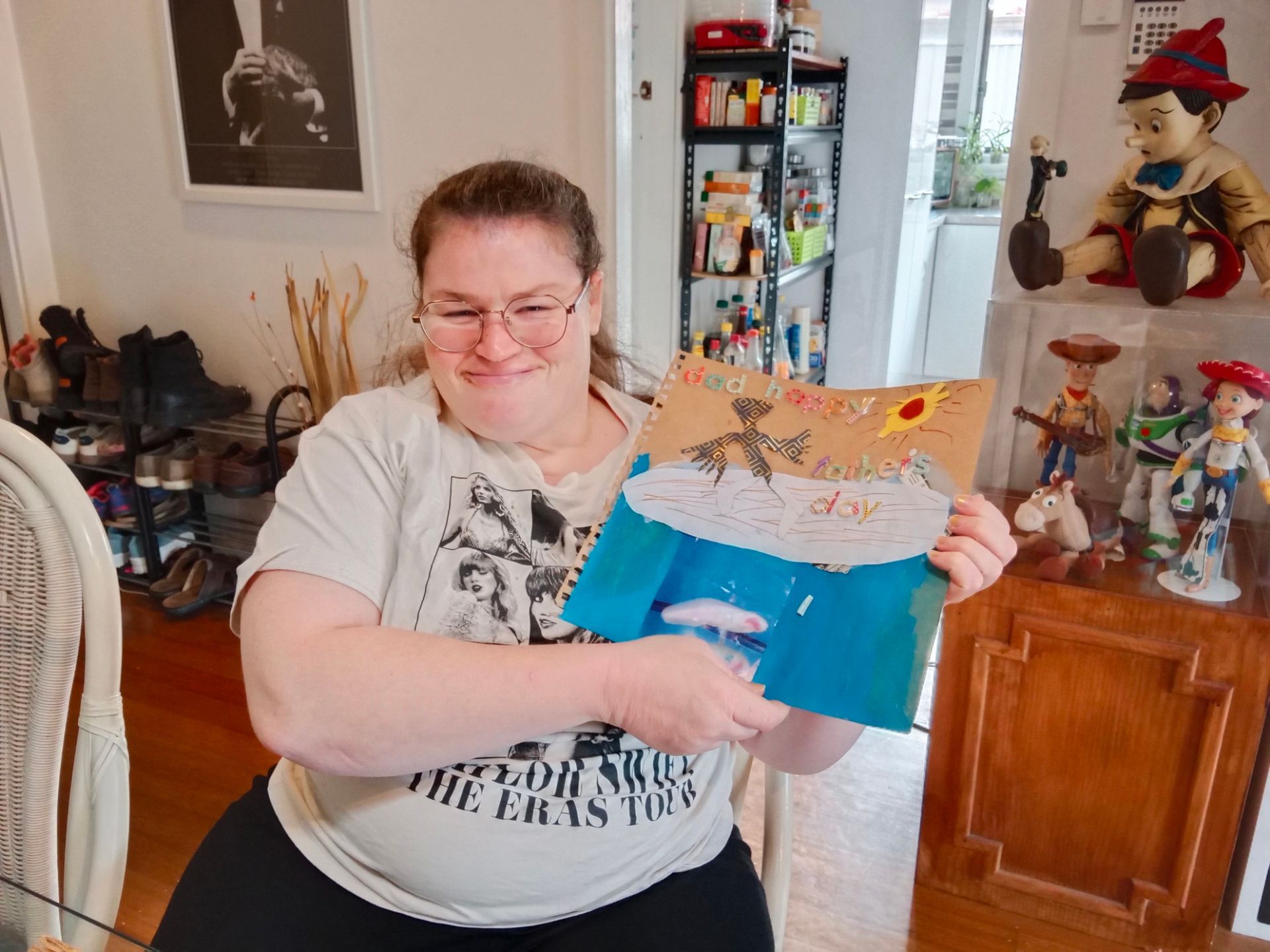 Woman holds up artwork; drawing of ocean, sun, and clouds; smiling; interior setting. — VAL Disability Services in Taree, NSW