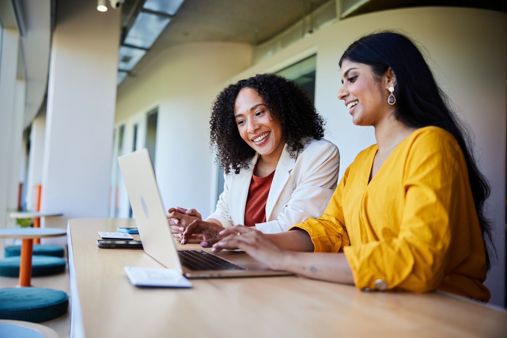 Two women are sitting at a table looking at a laptop computer.