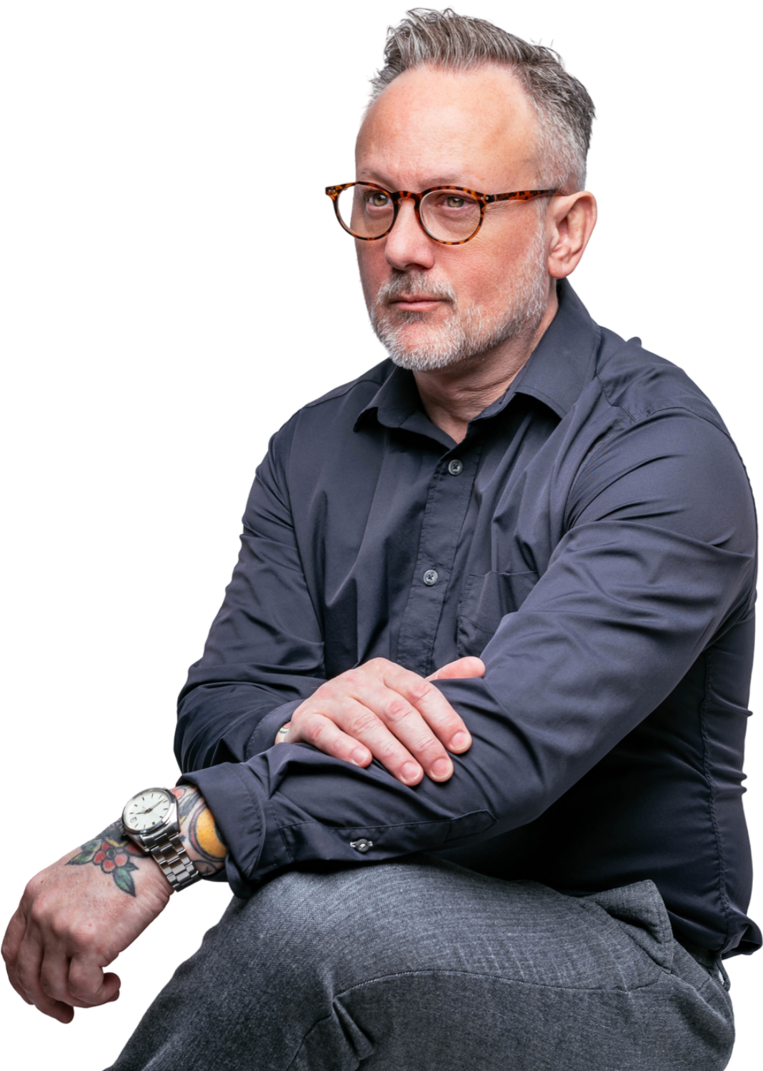 A man wearing glasses and a watch is sitting down with his arms crossed.