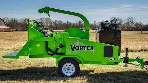 A green vortex tree chipper is parked on a trailer in a field.