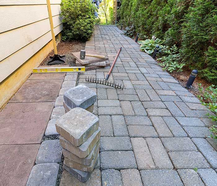 A stack of bricks is sitting on a sidewalk next to a rake.