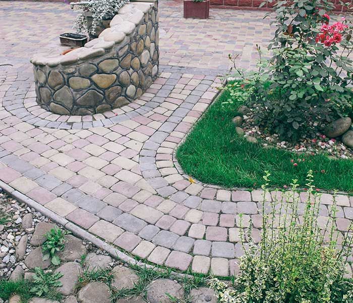 A stone wall surrounds a brick walkway in a garden.