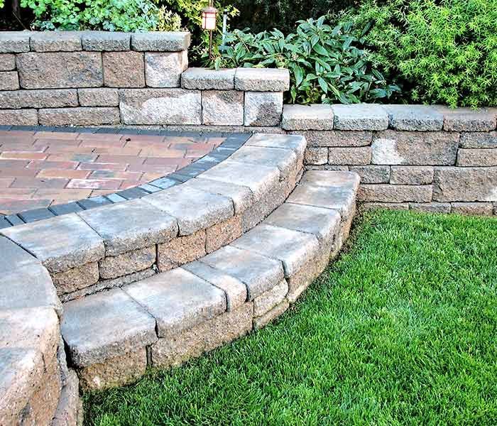 A stone wall with steps leading up to a brick patio.