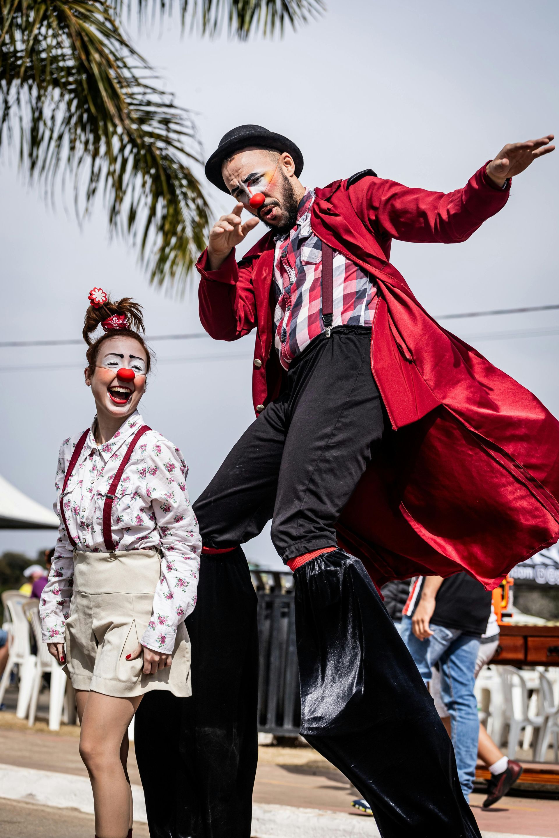 A man and a woman dressed as clowns are walking on stilts.