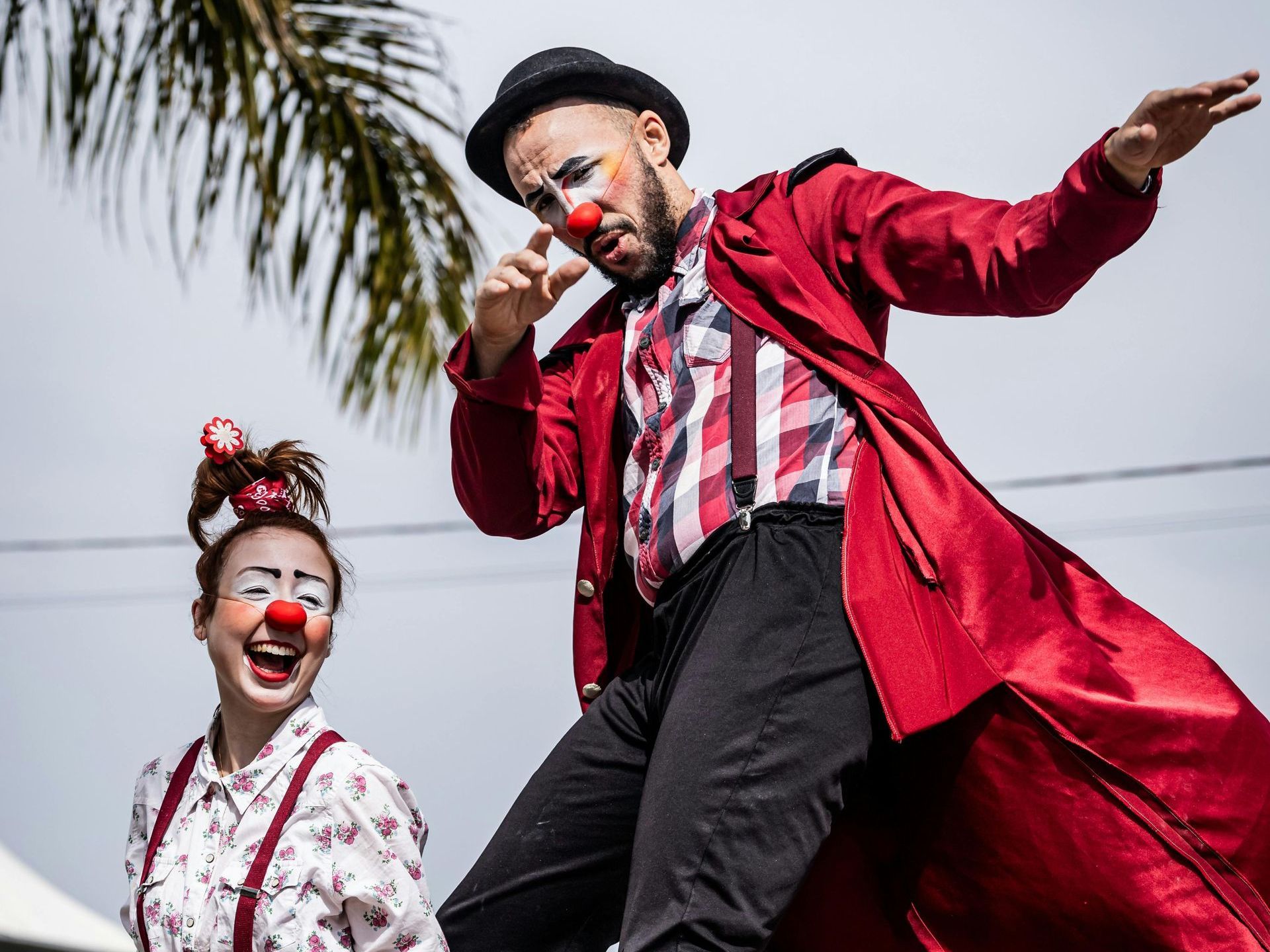 A man and a woman dressed as clowns are walking on stilts.