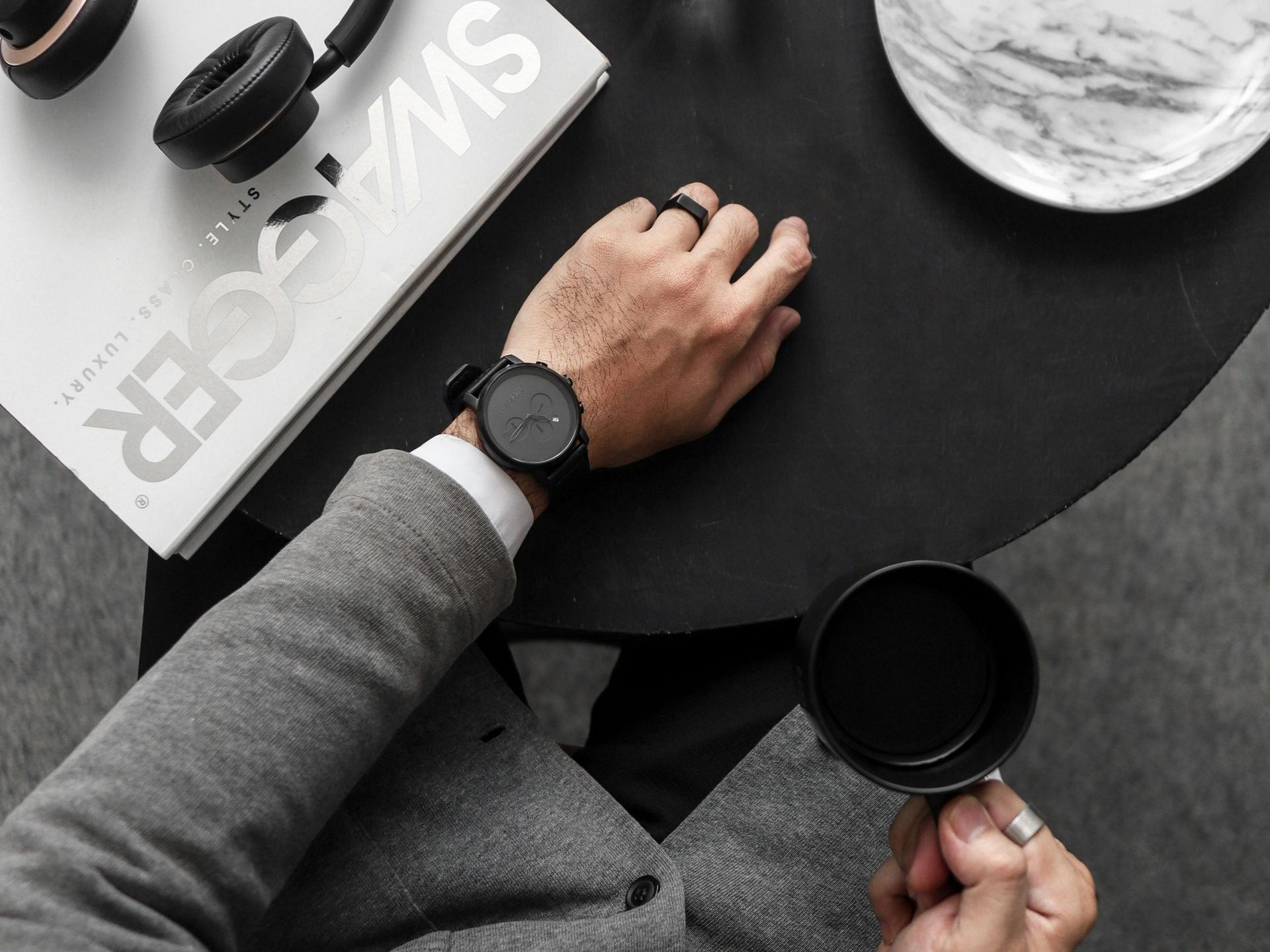 A man wearing a watch is sitting at a table holding a cup of coffee