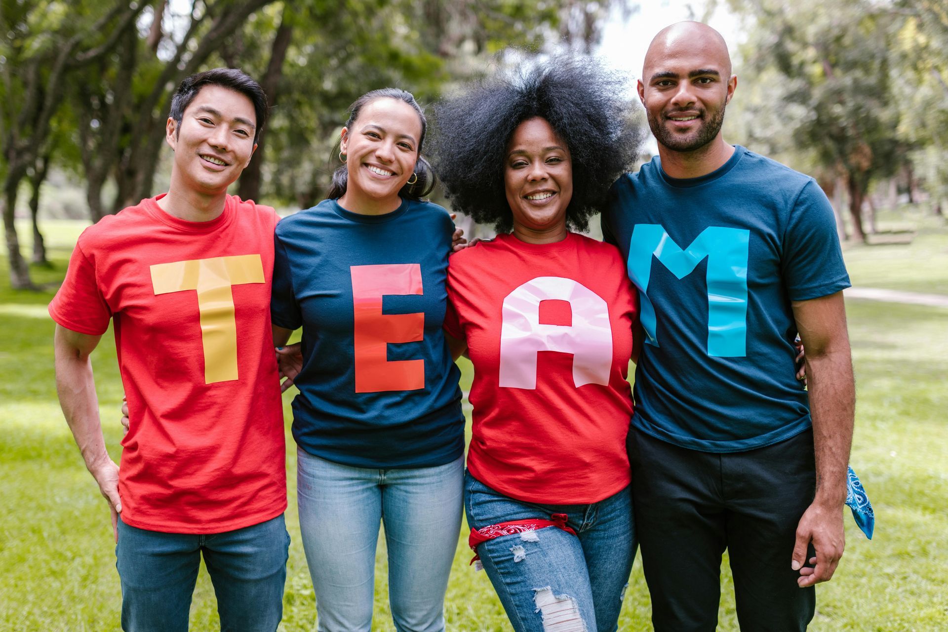 A group of people wearing team shirts are posing for a picture in a park.