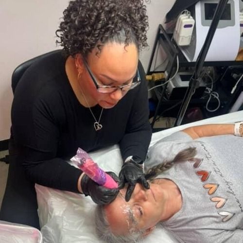A woman is getting a tattoo on a man 's forehead