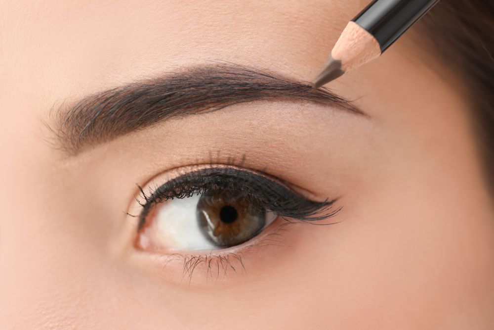 A woman is applying eyebrow pencil to her eyebrows.