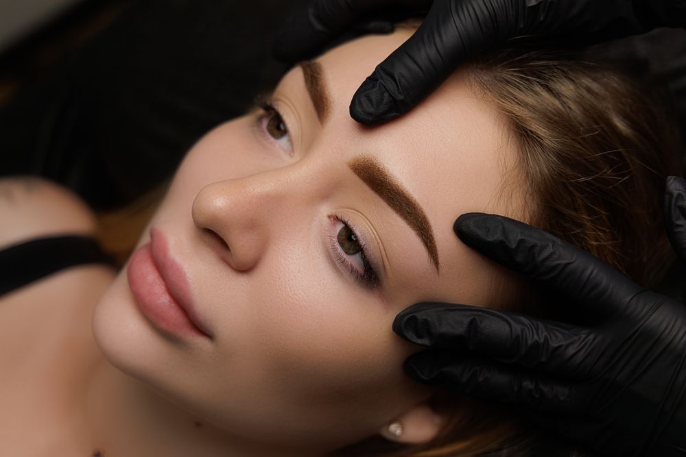 A woman is getting her eyebrows done by a person wearing black gloves.