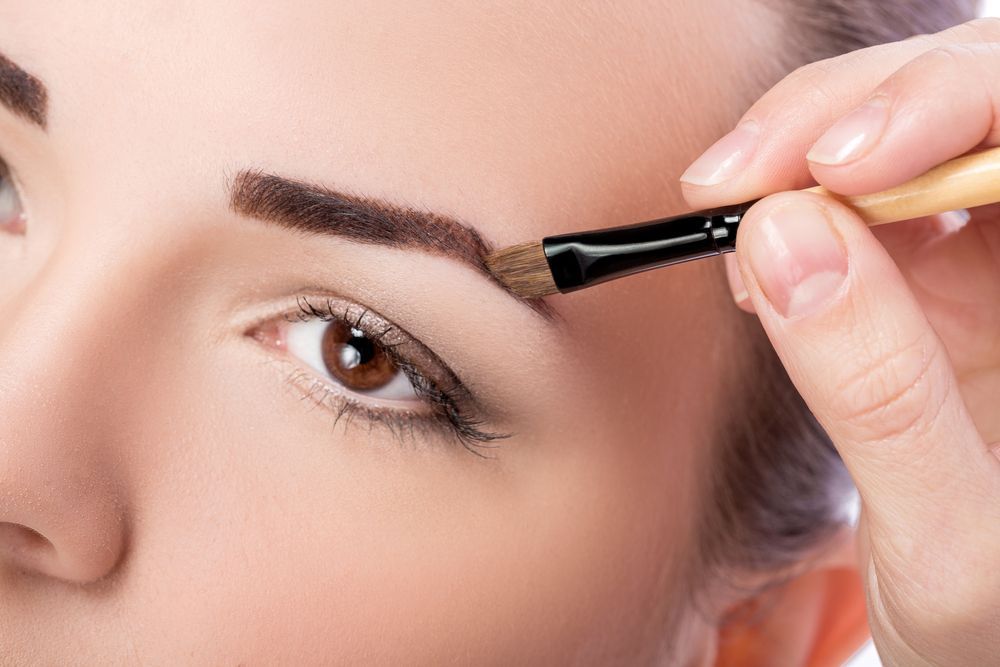 A woman is applying makeup to her eyebrows with a brush.