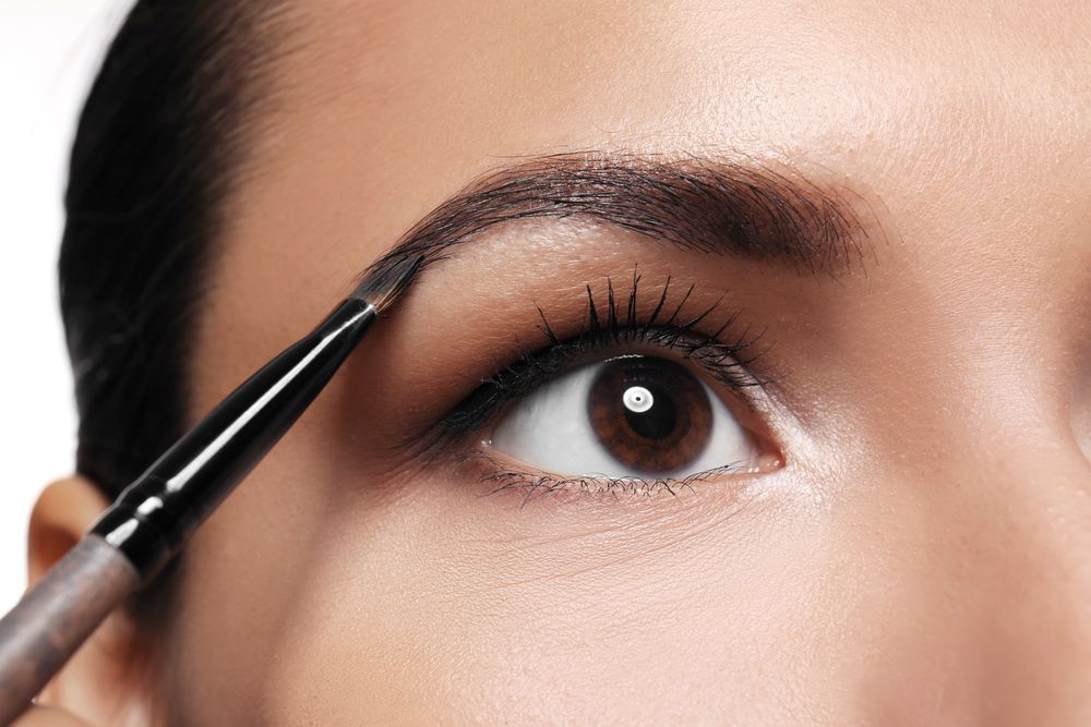 A woman is applying makeup to her eyebrows with a brush.