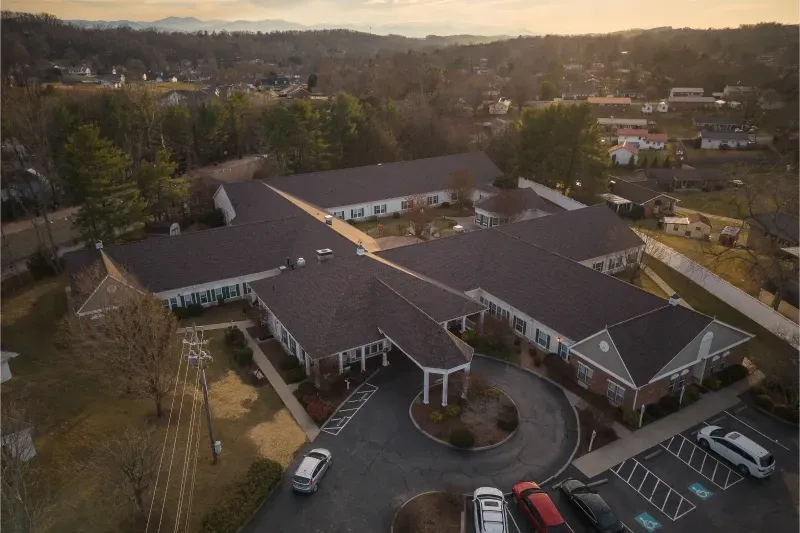 Aerial view of a large brown-roofed building with a circular drive and parked cars at sunset