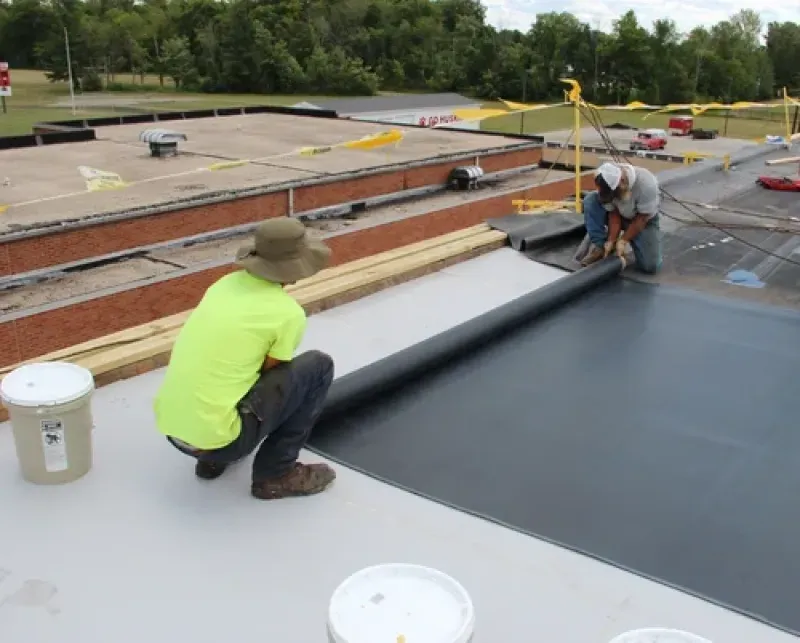 Workers installing black roofing membrane on a flat rooftop.