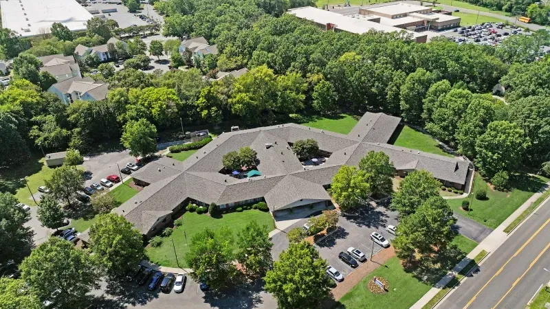 Aerial view of a long brown office building with parking lots, trees, and a road nearby.