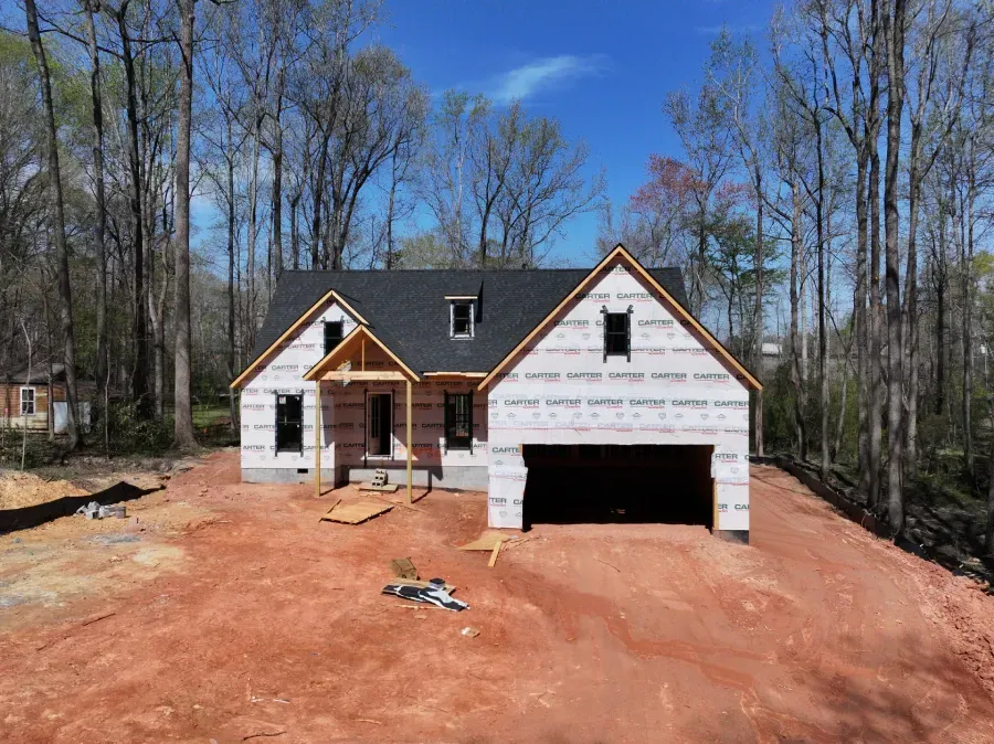 Newly built house with white siding, black roof, and red dirt yard in a wooded area