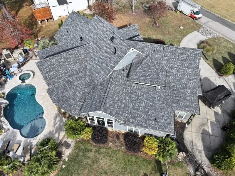 Aerial view of a house with a gray roof beside a curved backyard swimming pool and patio.
