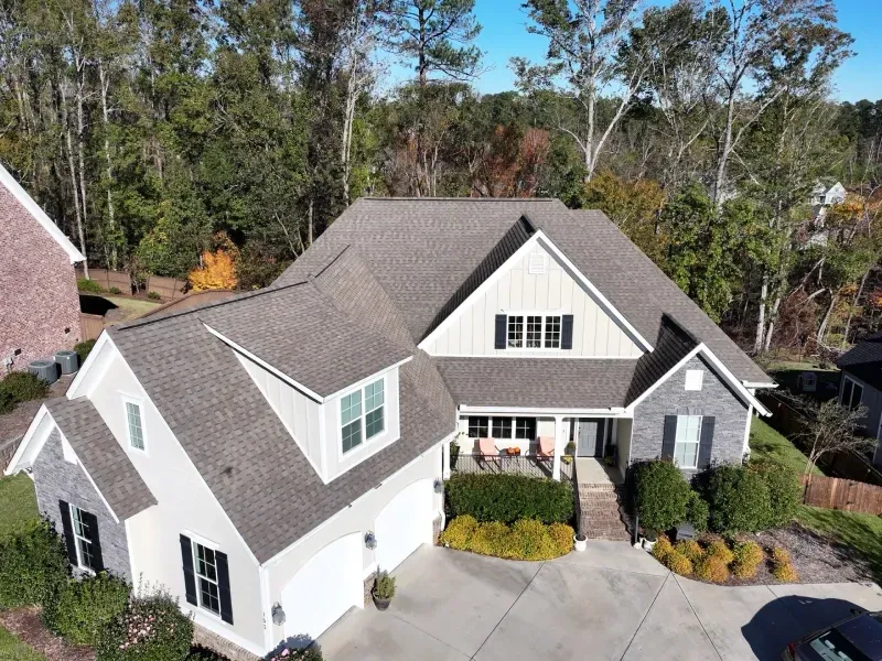 Aerial view of a gray suburban house with a front porch and landscaped yard