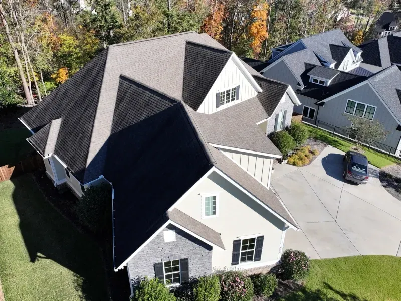 Aerial view of a suburban house with gray shingles, white siding, and a driveway with a parked car.