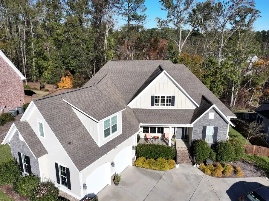 Aerial view of a white suburban house with gray roof, front landscaping, and trees behind it