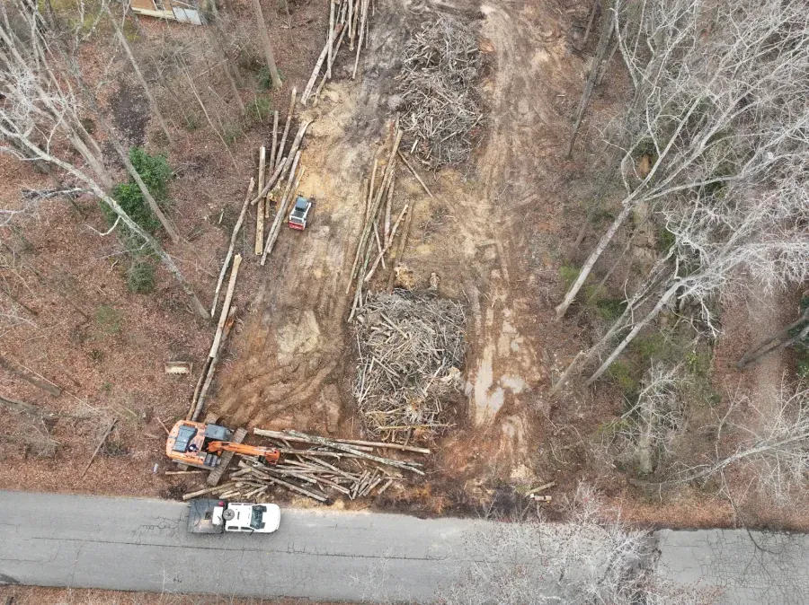 Aerial view of a roadside construction site with an excavator, truck, and cleared wooded area
