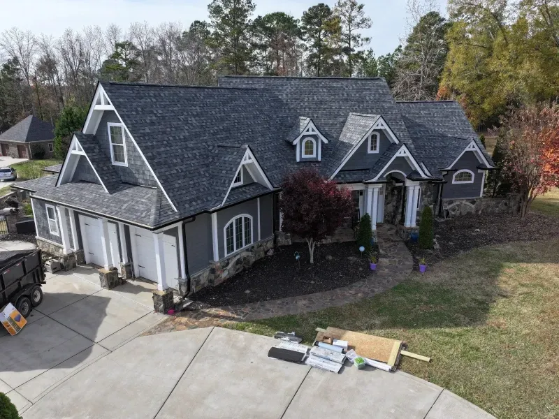 Aerial view of a gray house with a dark roof, front driveway, and scattered moving items on the lawn.