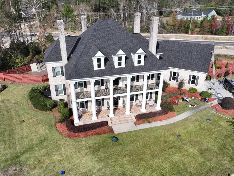 Aerial view of a large white house with a dark roof, wraparound porch, and manicured lawn.