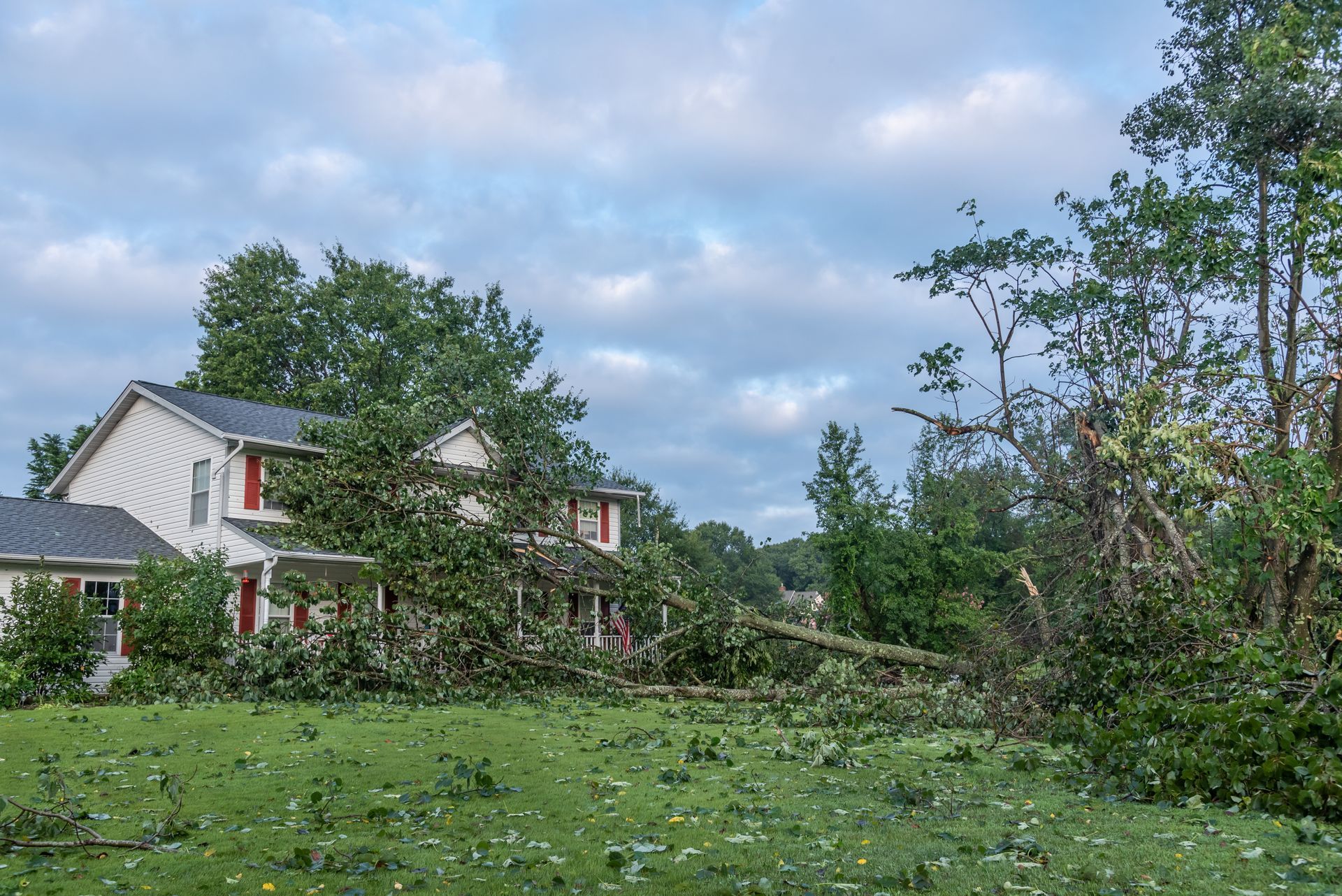 White house with red trim beside an overgrown green yard under a cloudy sky