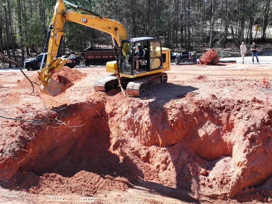 Yellow excavator digging a deep red dirt pit at a construction site