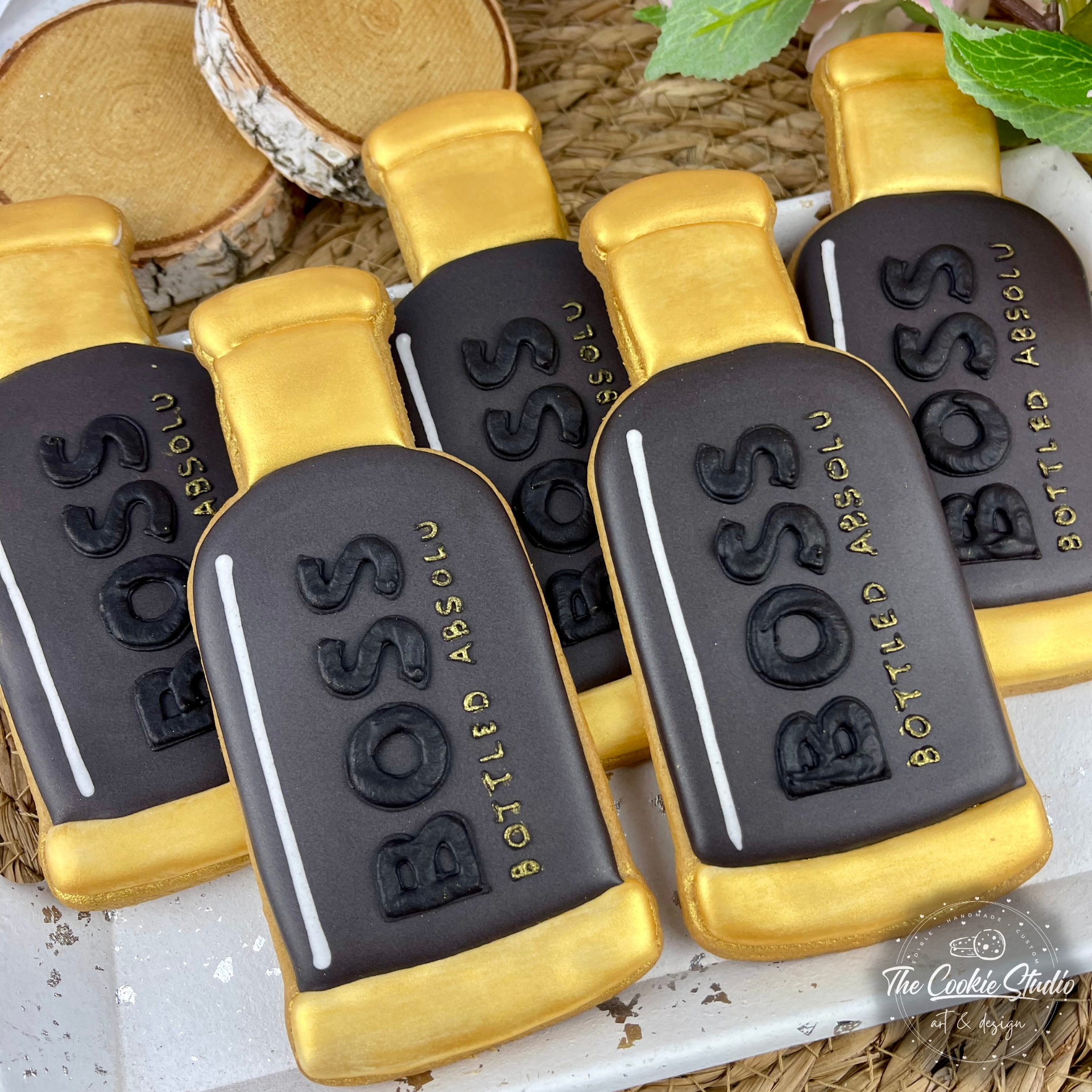 Koekjes versierd als Boss-parfumflesjes, donkergrijs met gouden accenten en letters.