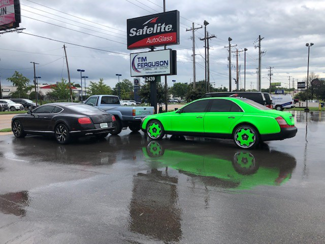 Two luxury cars parked: a green Maybach and a dark Bentley. Wet pavement reflects the scene. | Madison Automotive