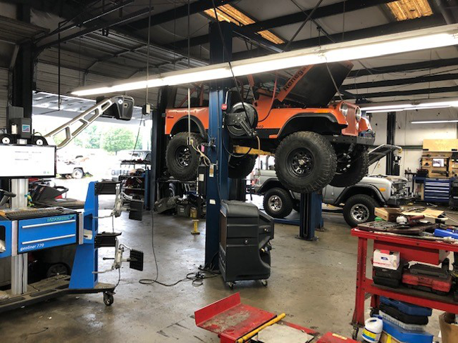 Orange Jeep raised on a lift in a garage; another Jeep visible. Alignment machine. | Madison Automotive
