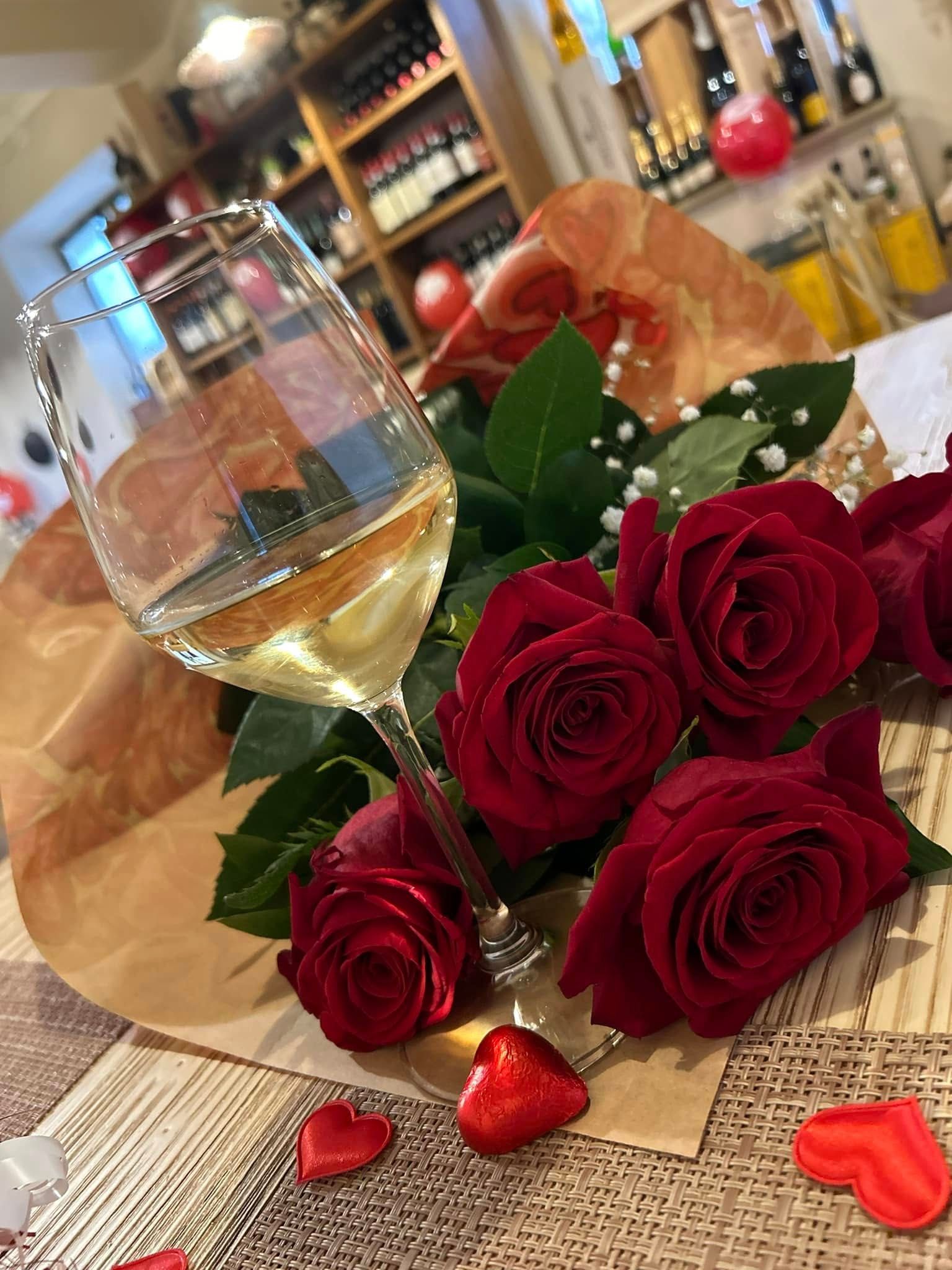 Un mazzo di rose rosse e un bicchiere di vino su un tavolo.