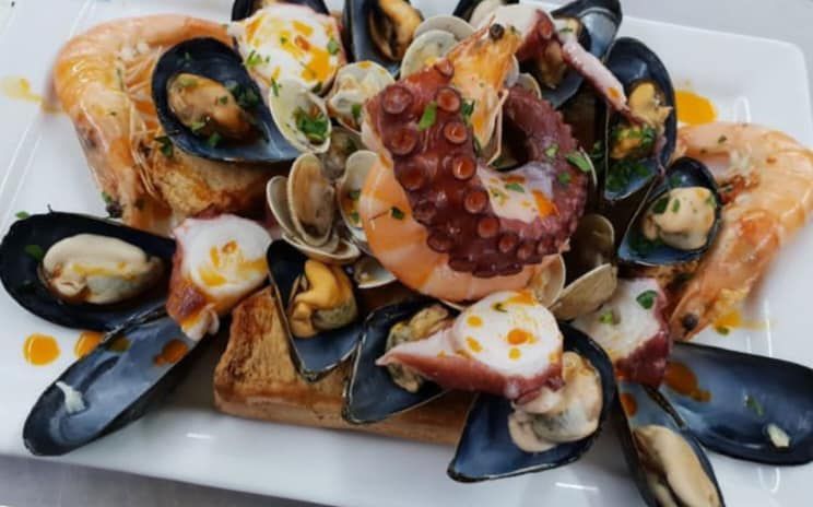 Un piatto bianco guarnito con frutti di mare, tra cui gamberi, cozze e polpo.