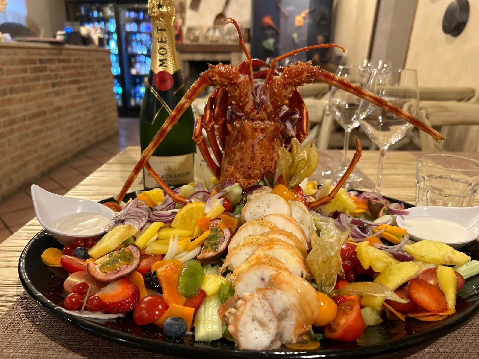 Un piatto di cibo con un'aragosta sopra e una bottiglia di champagne sullo sfondo.