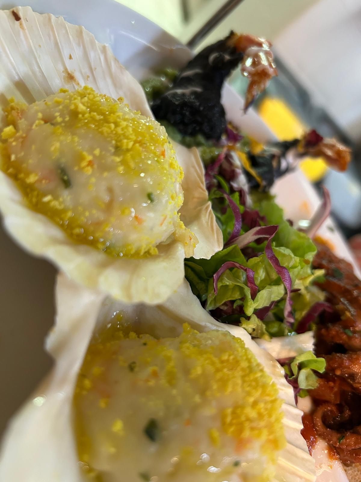 Un primo piano di un piatto di cibo con capesante e insalata.