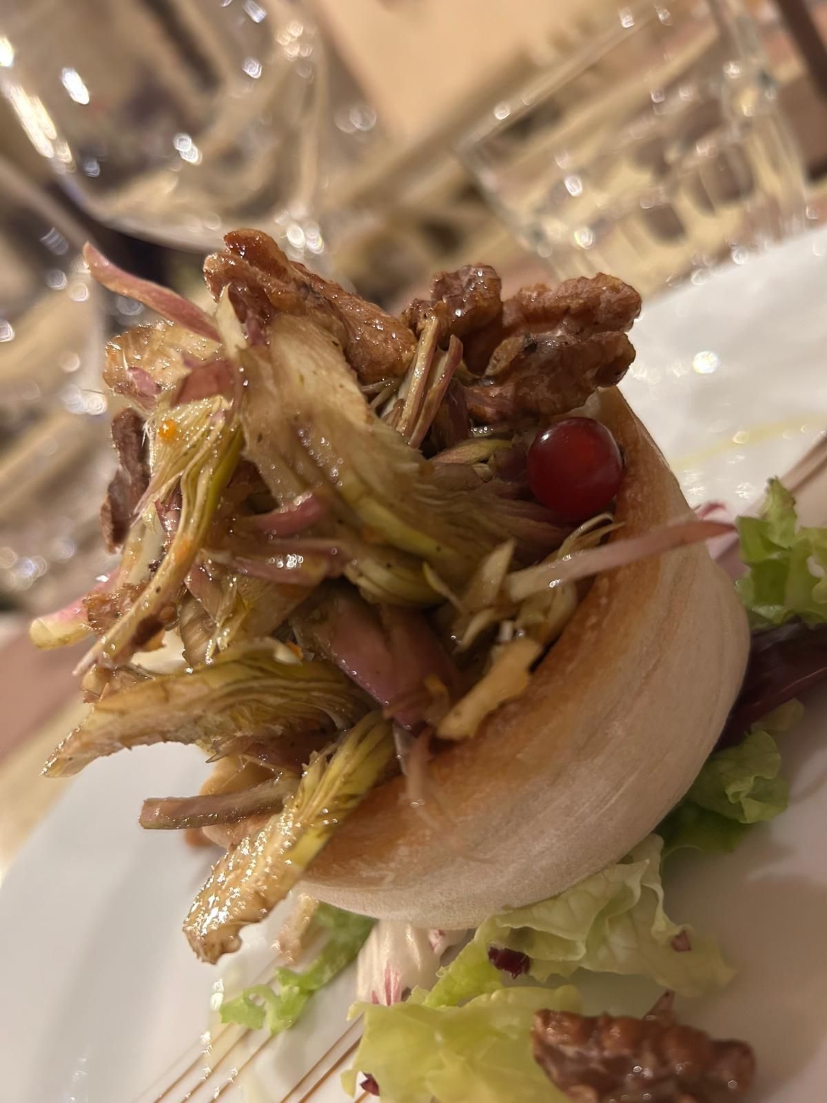Un primo piano di un'insalata su un piatto con un bicchiere di vino sullo sfondo.