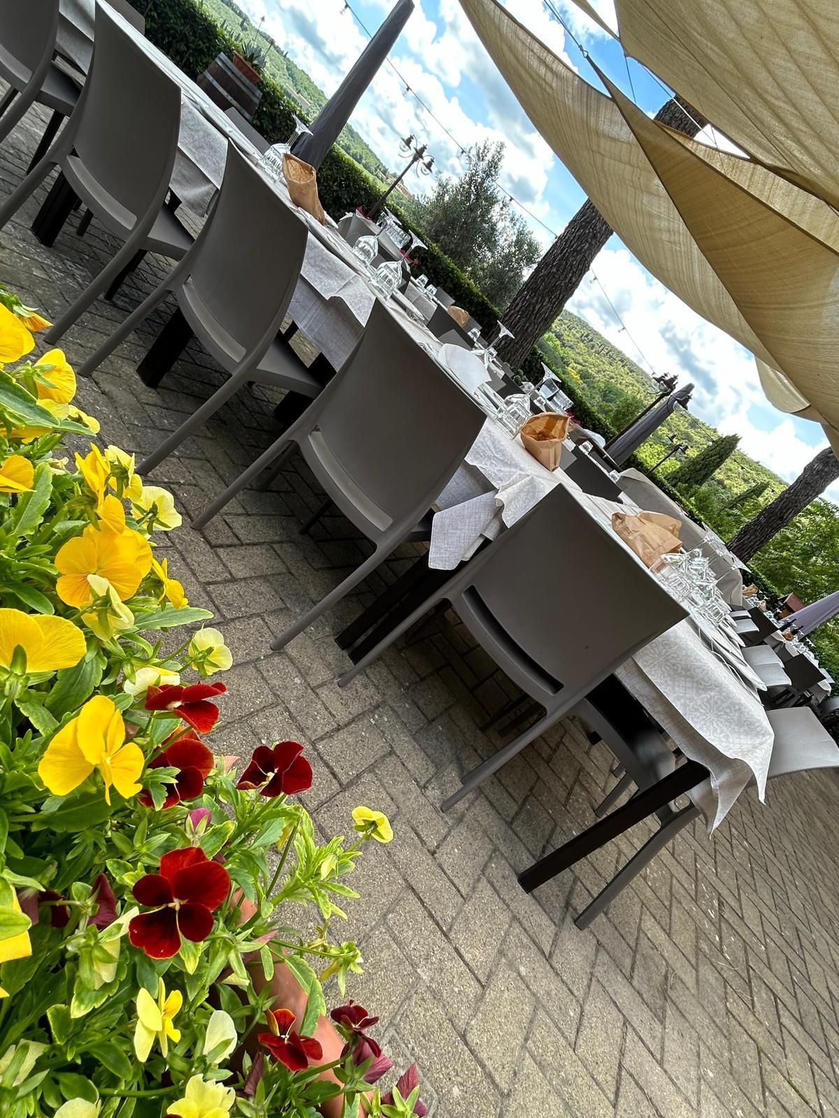 Un patio con tavoli, sedie e fiori in primo piano.