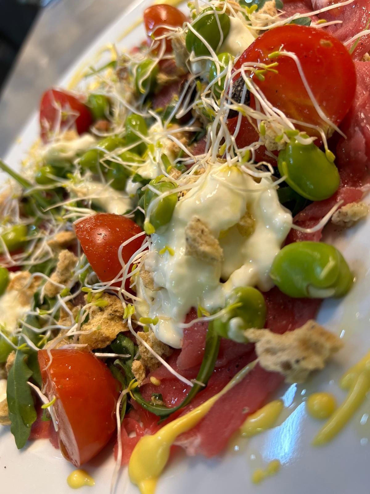 Un primo piano di un piatto di cibo con pomodori e germogli su un tavolo.