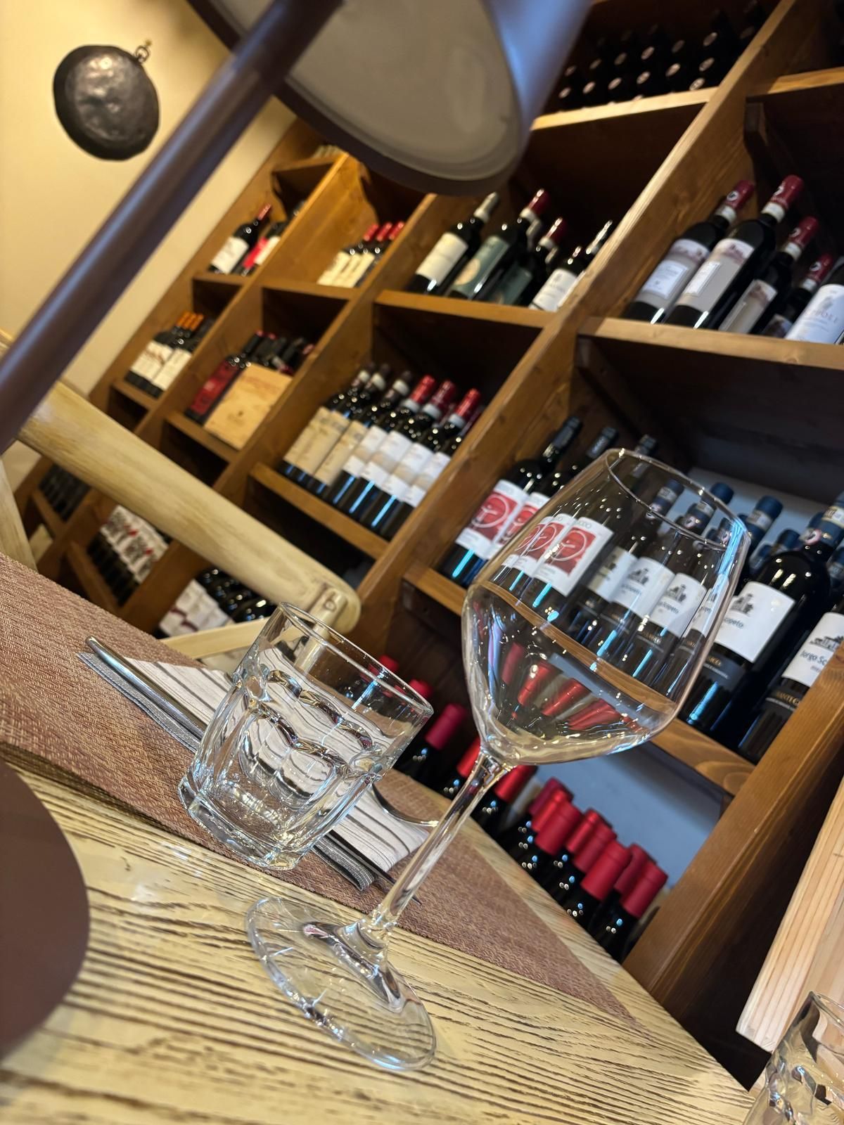 Un bicchiere di vino è appoggiato su un tavolo davanti a uno scaffale pieno di bottiglie di vino