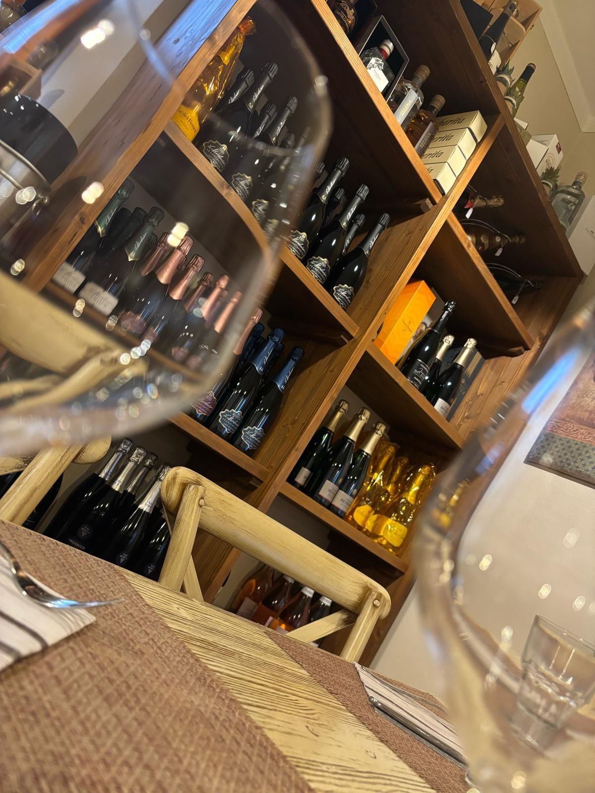 Un bicchiere di vino è appoggiato su un tavolo davanti a uno scaffale pieno di bottiglie di vino.