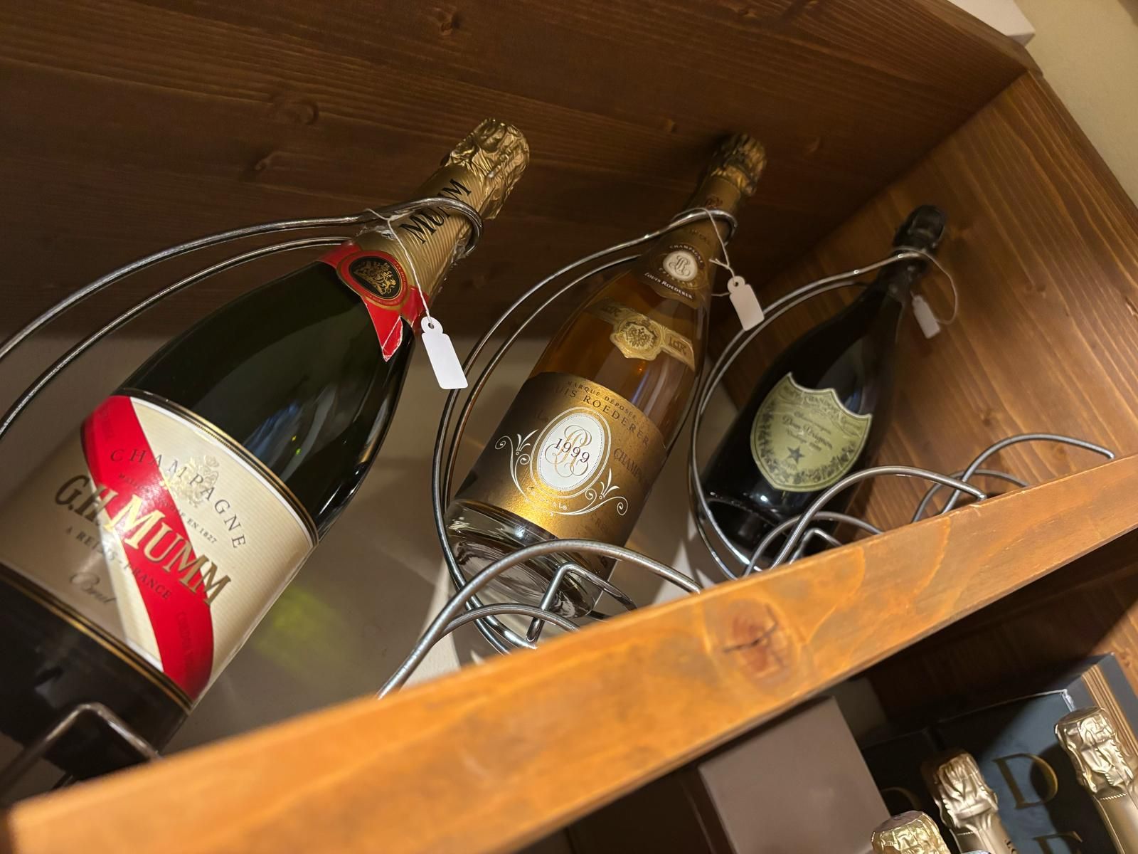 Tre bottiglie di champagne sono appoggiate su uno scaffale di legno.