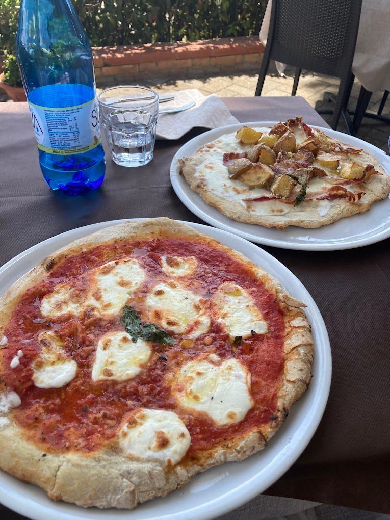 Due pizze sono appoggiate su un tavolo accanto a una bottiglia d'acqua.