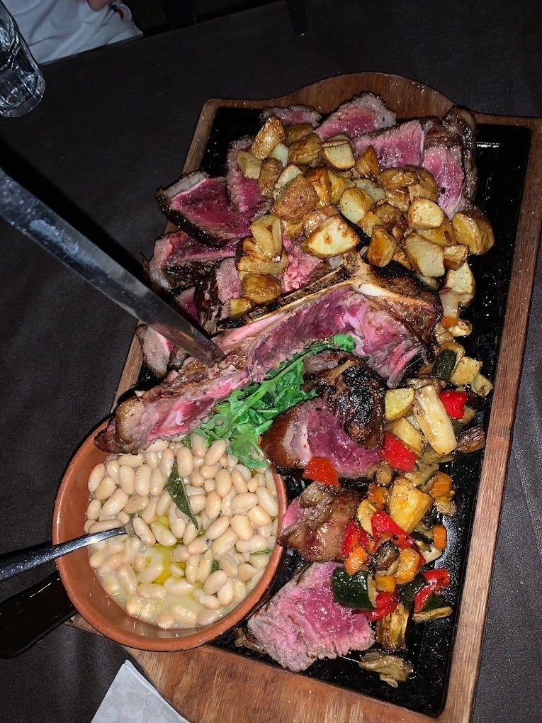 Un grosso pezzo di carne è appoggiato su un tagliere di legno accanto a una ciotola di fagioli.