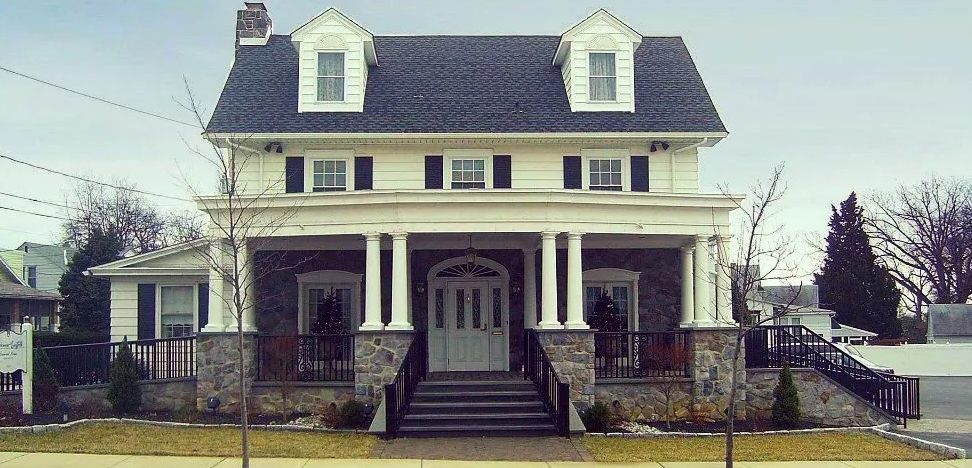 Two-story house with stone accents, a porch with white columns, and a dark gray roof.