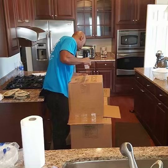 A man in a blue shirt is standing next to a cardboard box in a kitchen