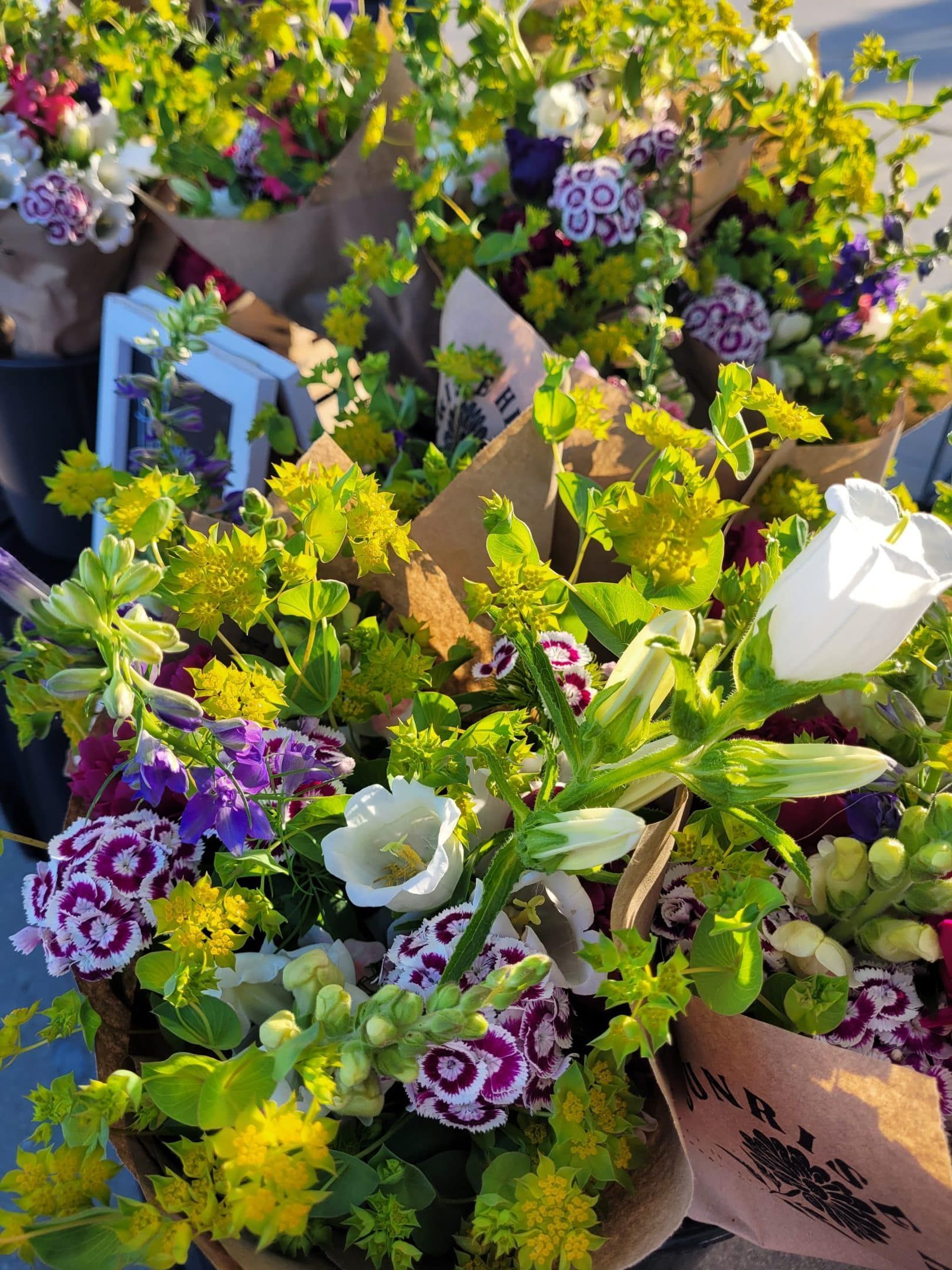 Bundles of colorful flowers wrapped in brown paper, including yellow, purple, and white blooms.