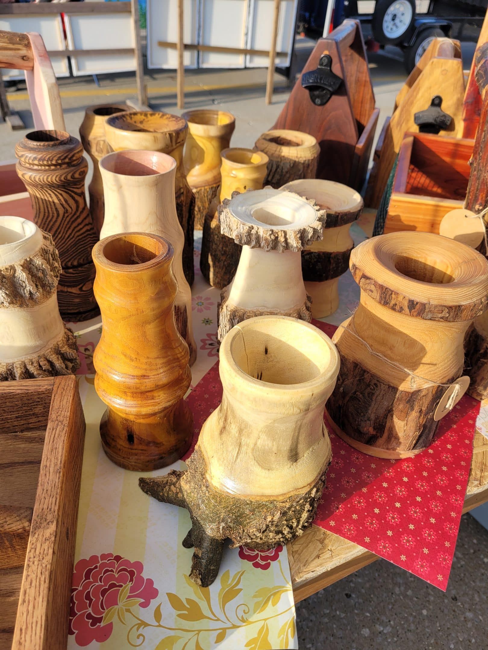 Wooden vases and bottle openers displayed on a table at an outdoor market. Some vases have rough bark edges.