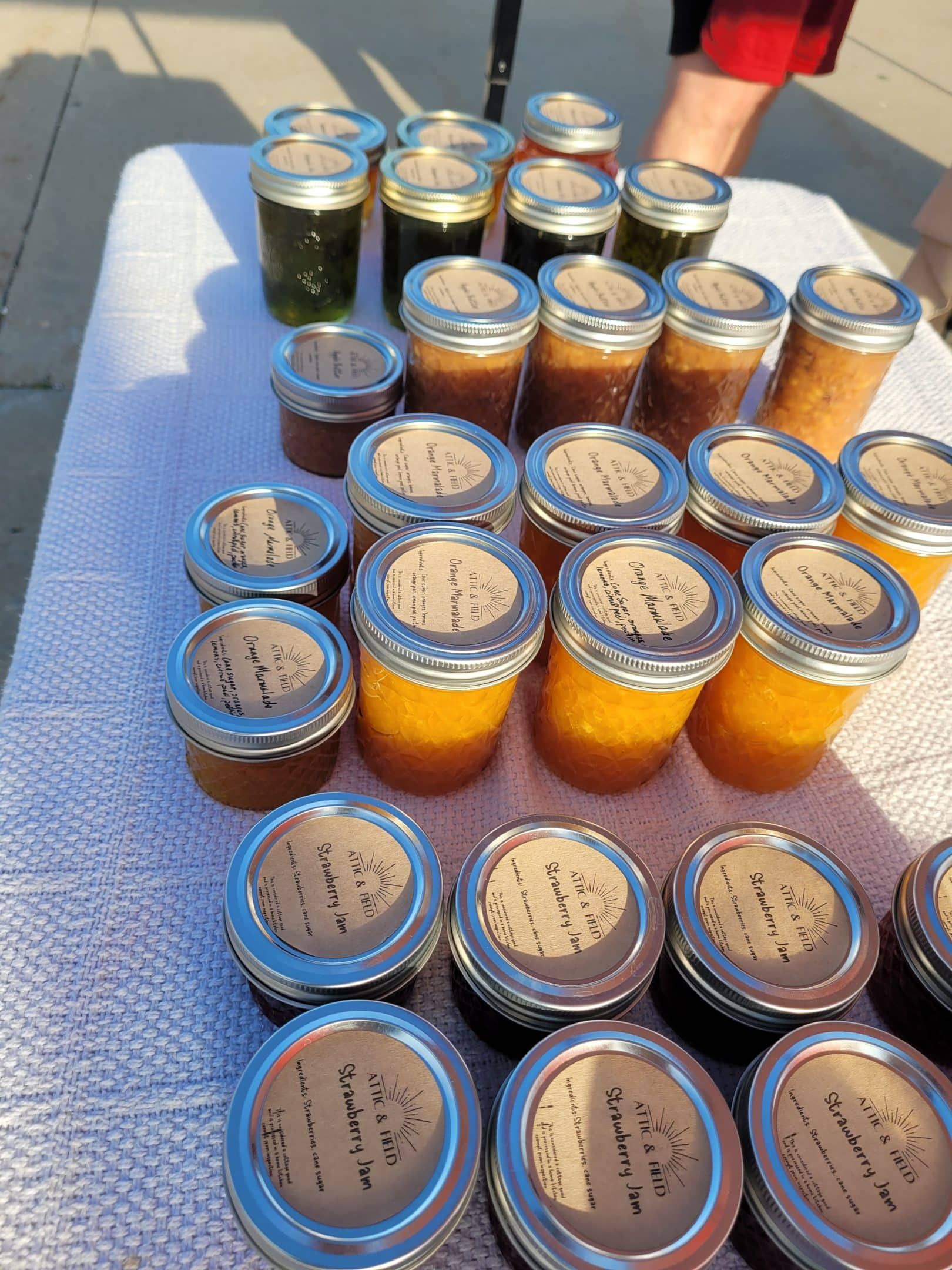 Jars of homemade jam and jelly on display at a market, in varying colors like orange, green, and dark red.